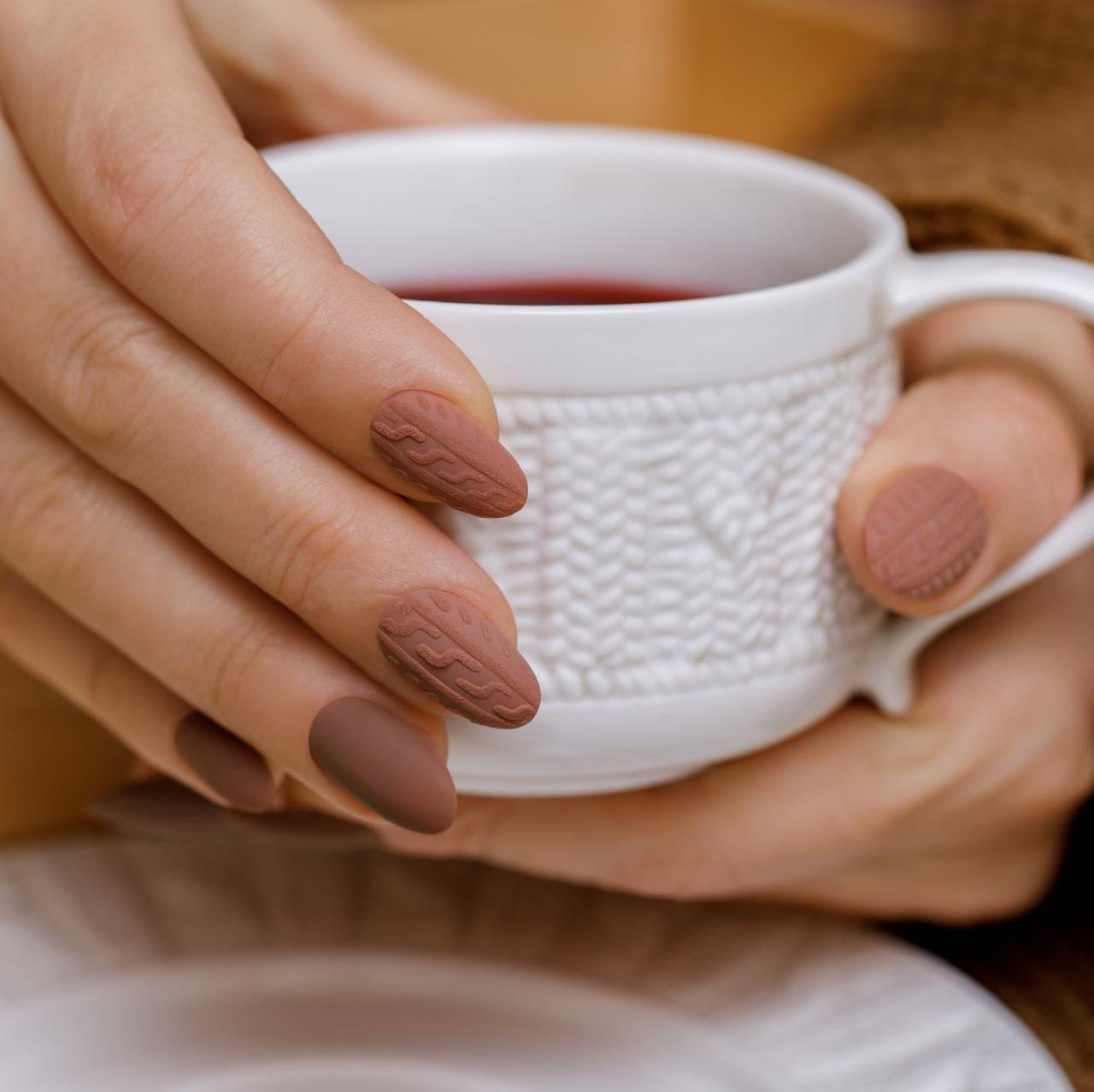 stylish winter nail design knitted fabric texture on women's nails a woman's hand holds a cup of warm drink