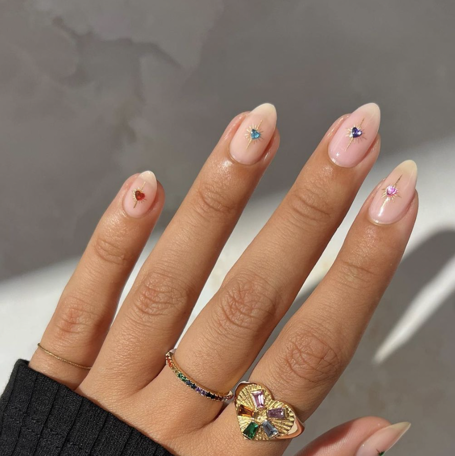 a hand with a ring on it and jeweled manicure