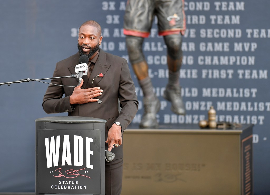 Dwyane Wade, former Miami Heat player, speaking into a microphone at his statue unveiling ceremony outside Kaseya Center in Miami, Florida