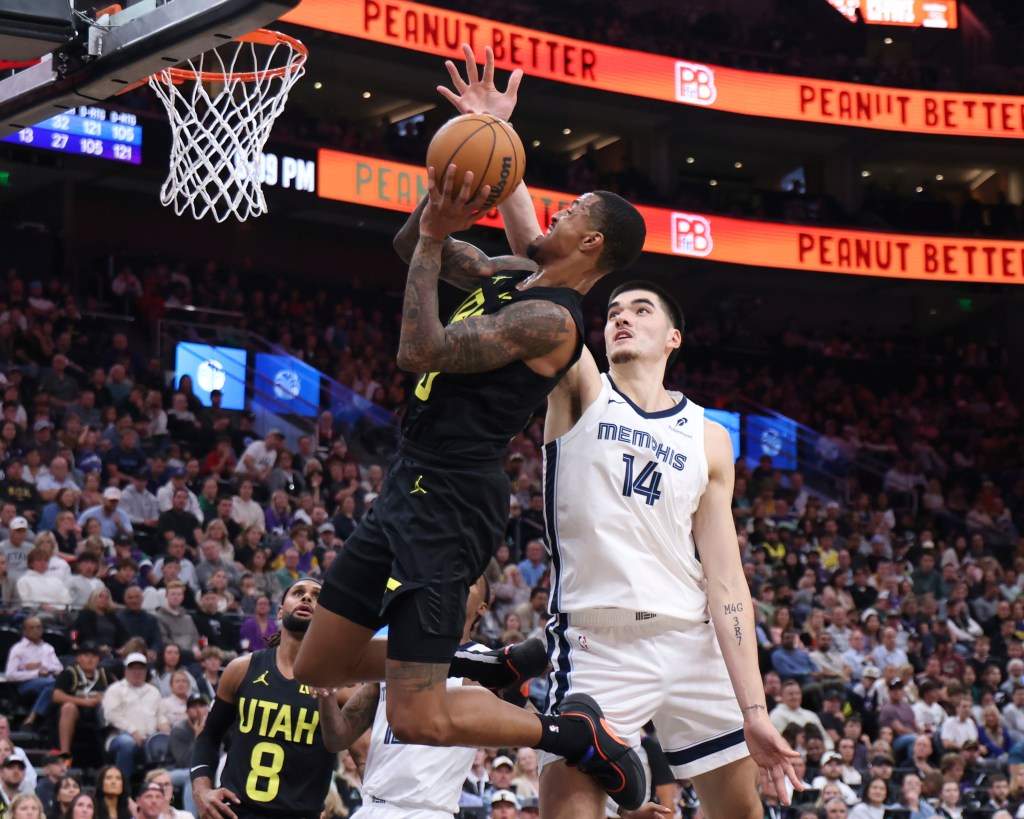 Utah Jazz forward John Collins (20) making a basket against Memphis Grizzlies center Zach Edey (14) during an NBA game, crowd and various celebrities in the background.